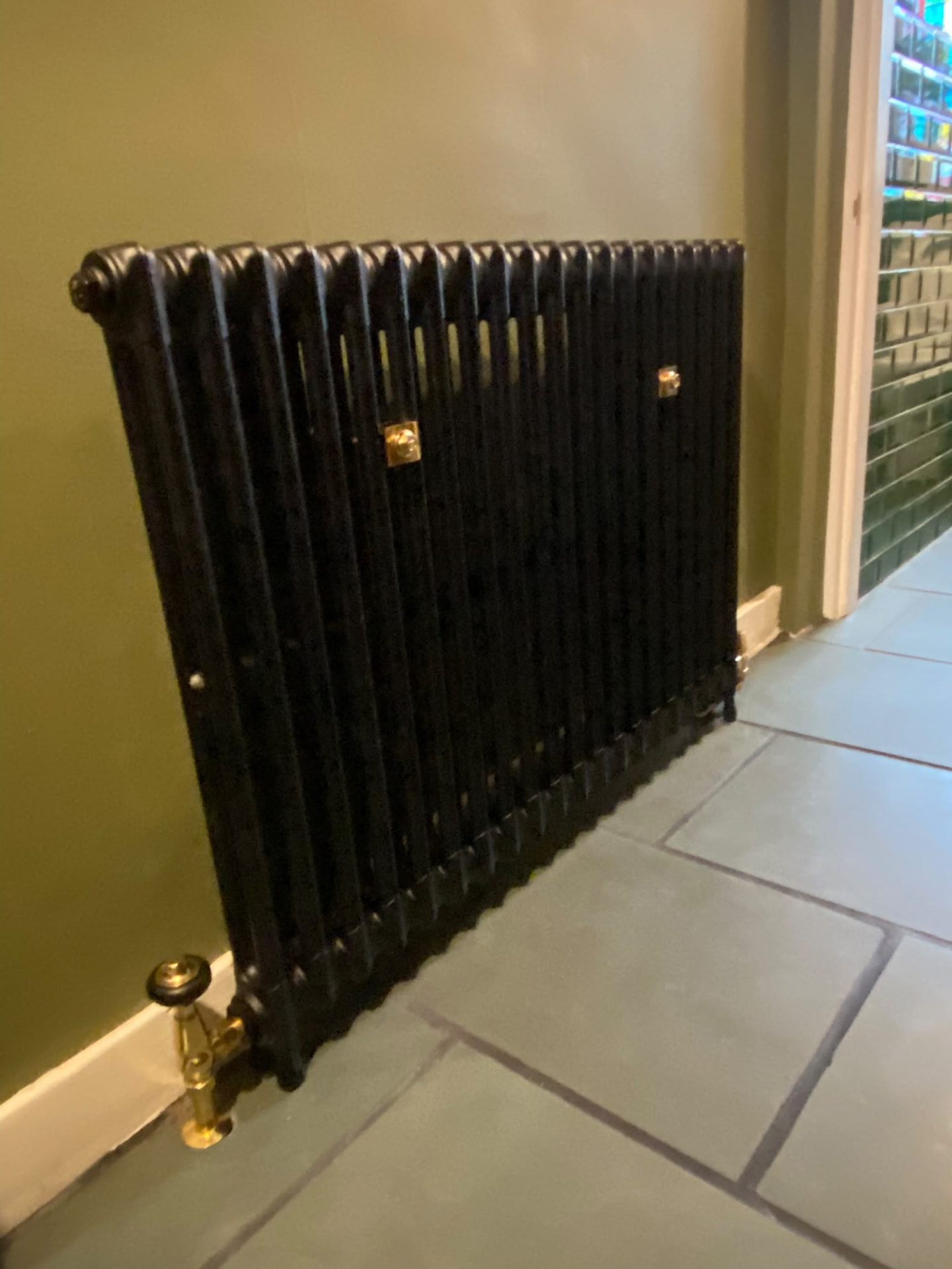 Side view of a cast iron column radiator next to green wall tiles in a London home