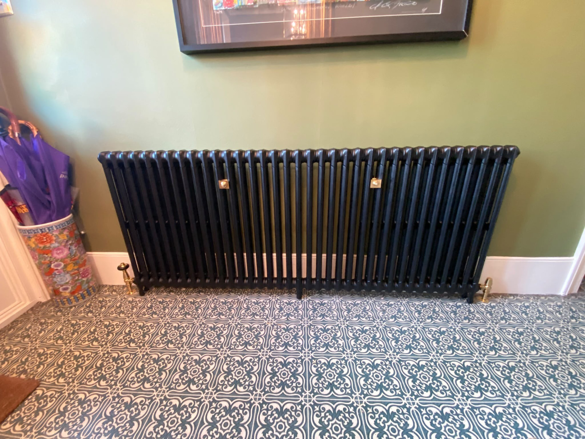 Straight-on view of a black cast iron column radiator on patterned London flooring